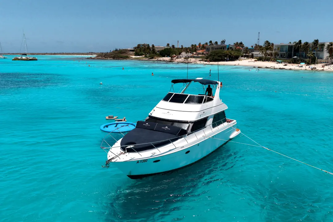 Vista de drone do Eden Luca Blue ancorado em frente a uma praia de Aruba, com o solário de proa azul-marinho sobre água turquesa