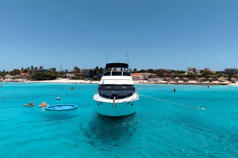 Eden Luca Blue head-on at anchor, the SunChill float and a white-sand Aruba beach behind