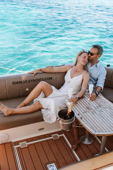 Casal relaxando na popa de um iate Eden Luca com champanhe e água turquesa ao fundo