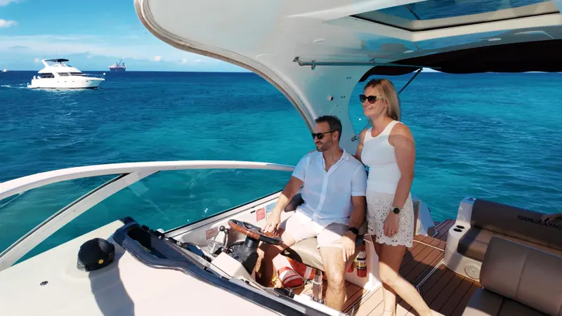 Couple at the helm of Eden Luca Red in turquoise water, Eden Luca Blue cruising behind