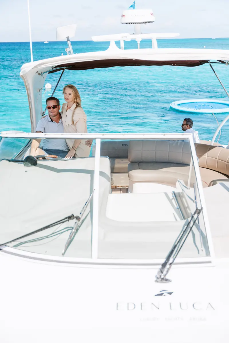 Couple at the helm of Eden Luca Red seen from the bow, the SunChill float in the water behind