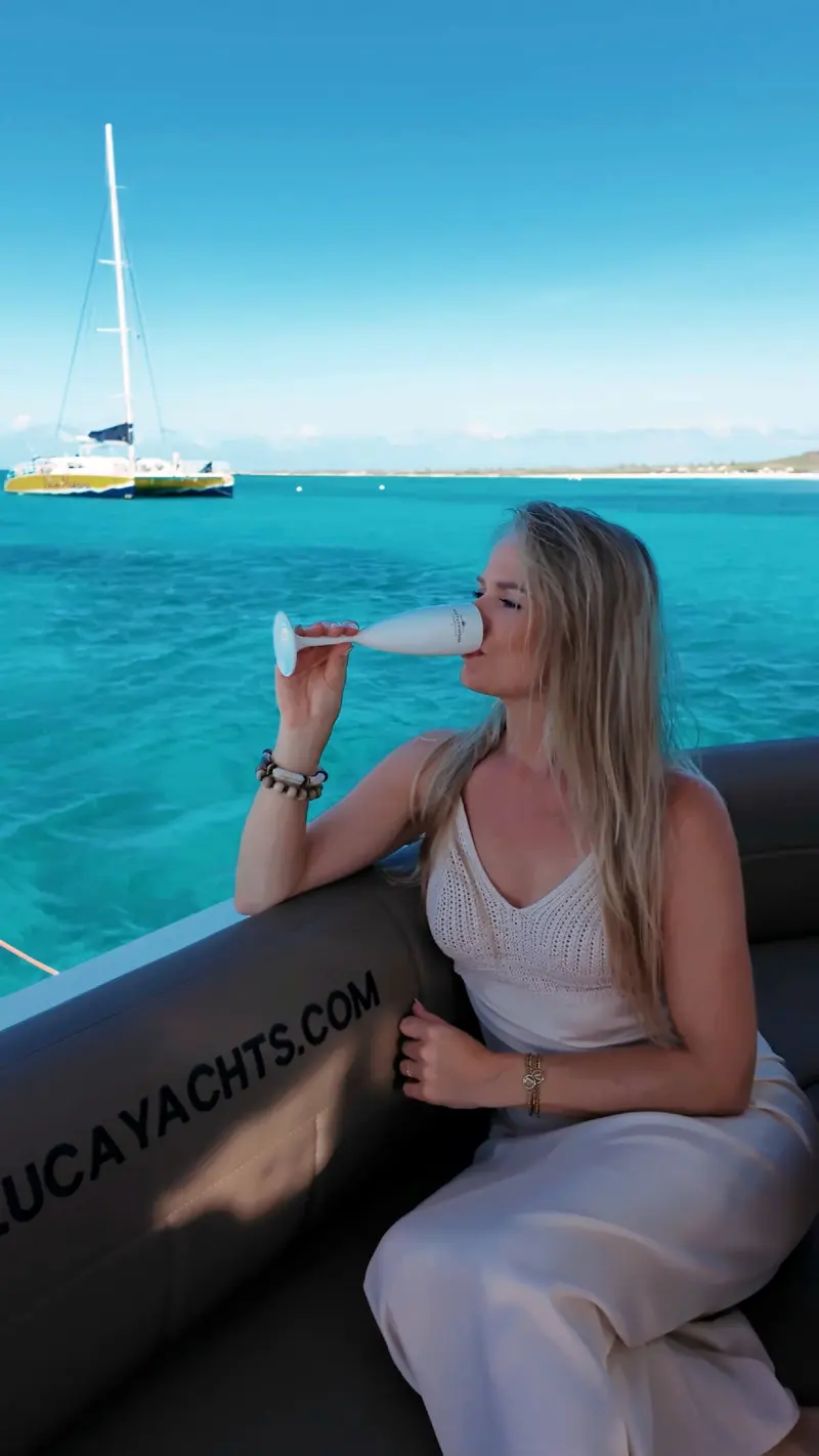 Guest raising a glass of bubbly on Eden Luca Red, a catamaran on the turquoise water behind