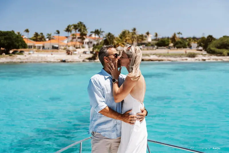 Newly engaged couple embracing on the bow, a palm-lined Aruba beach behind them
