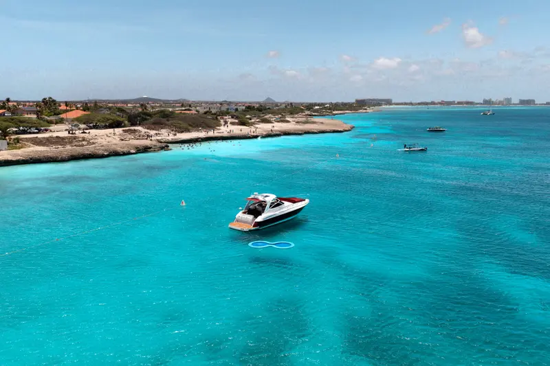 Wide drone view of Eden Luca Red anchored along Aruba's coastline in vivid turquoise water
