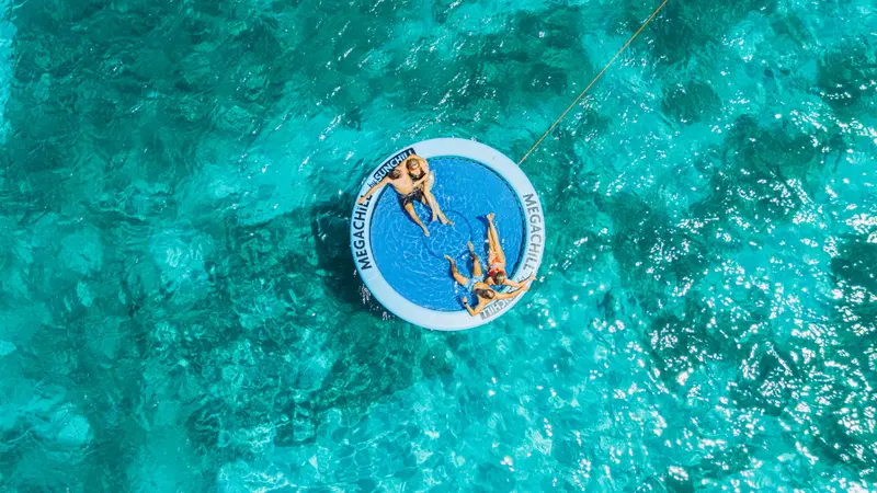 Drone view of a couple on the SunChill floating lounge behind an Eden Luca yacht in Aruba