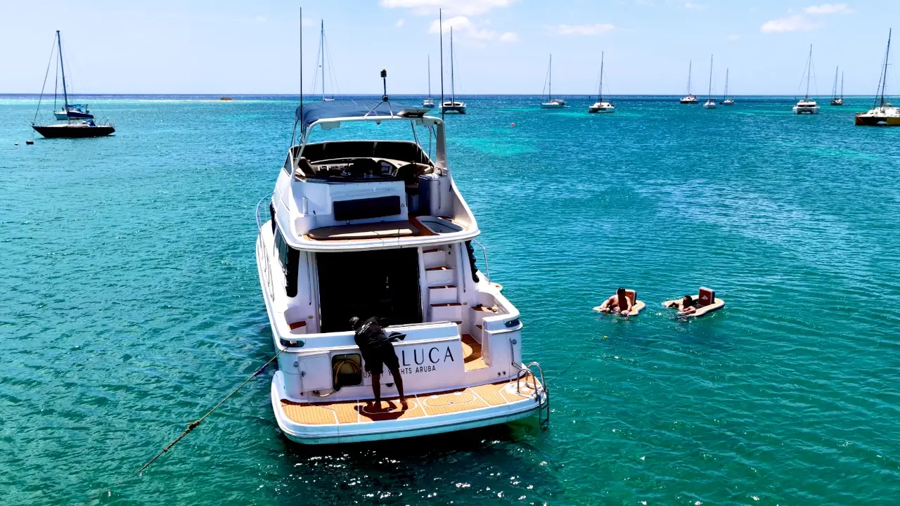 Guests floating in turquoise water beside Eden Luca Blue at anchor off an Aruba beach