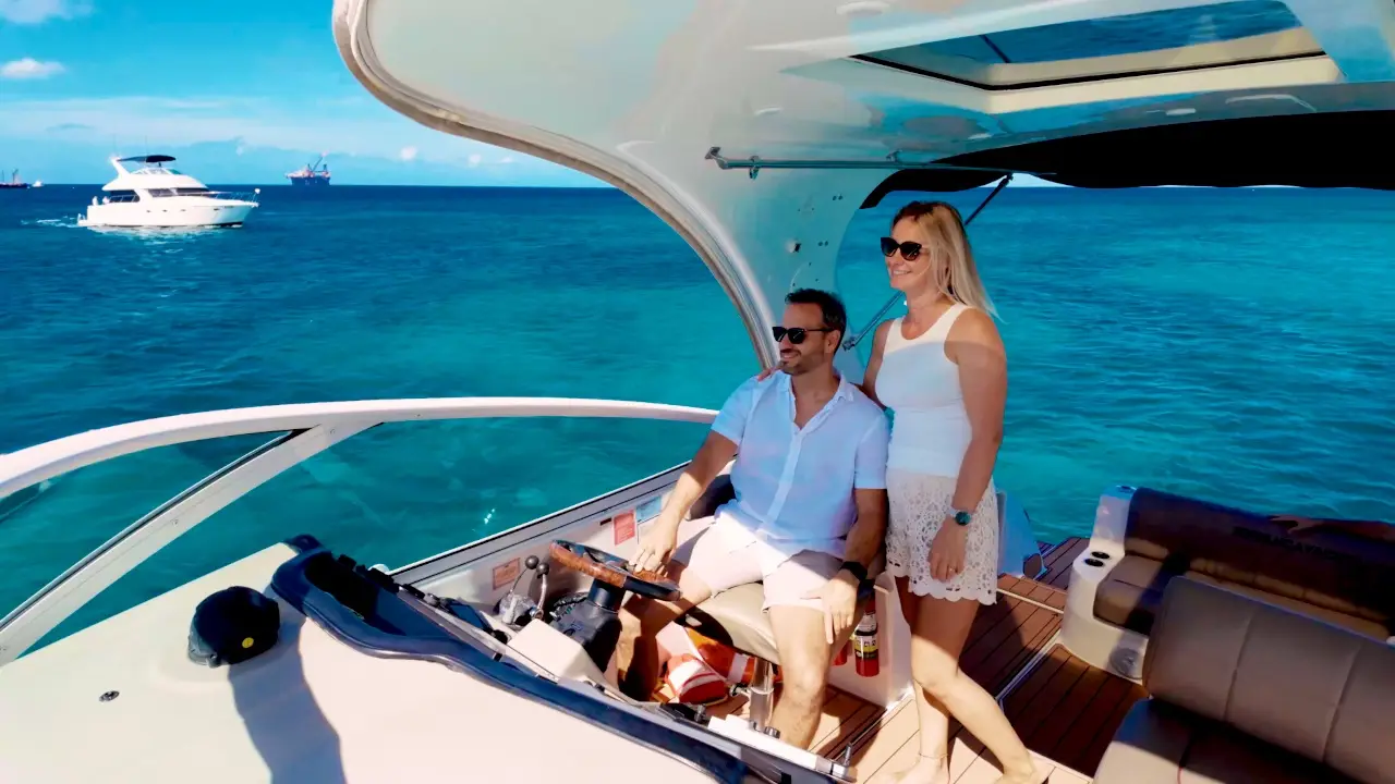 Couple at the helm of Eden Luca Red in turquoise water, Eden Luca Blue cruising behind