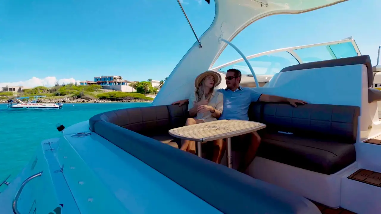 Couple relaxing in the cockpit lounge of Eden Luca Red at anchor, a palm-lined shore behind