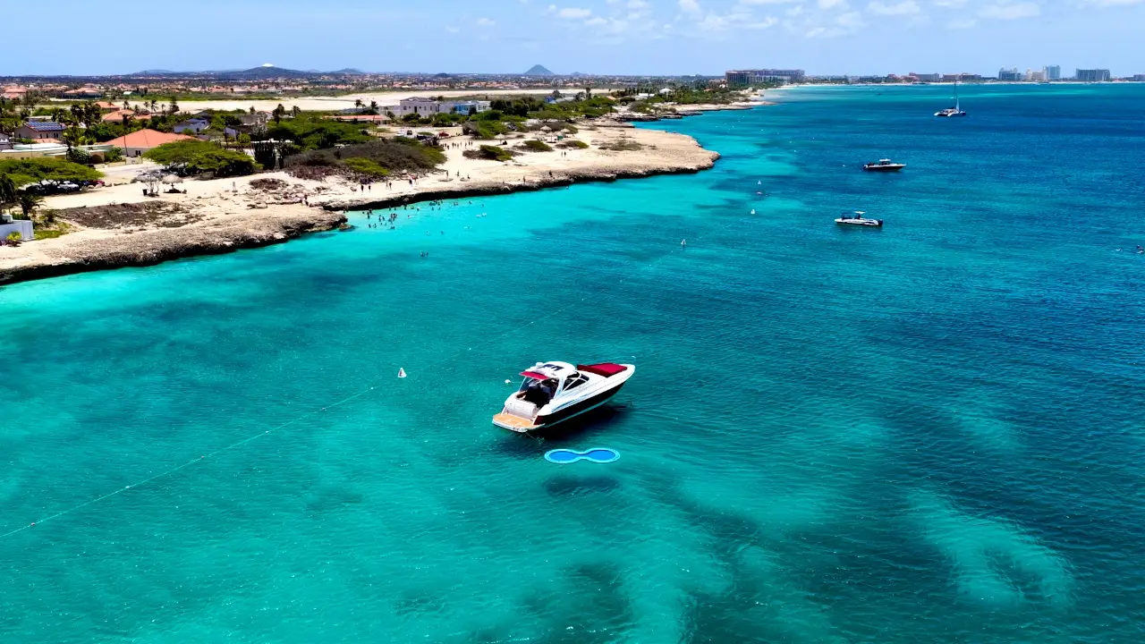 Drone flying over Eden Luca Red at anchor in turquoise water along Aruba's coastline